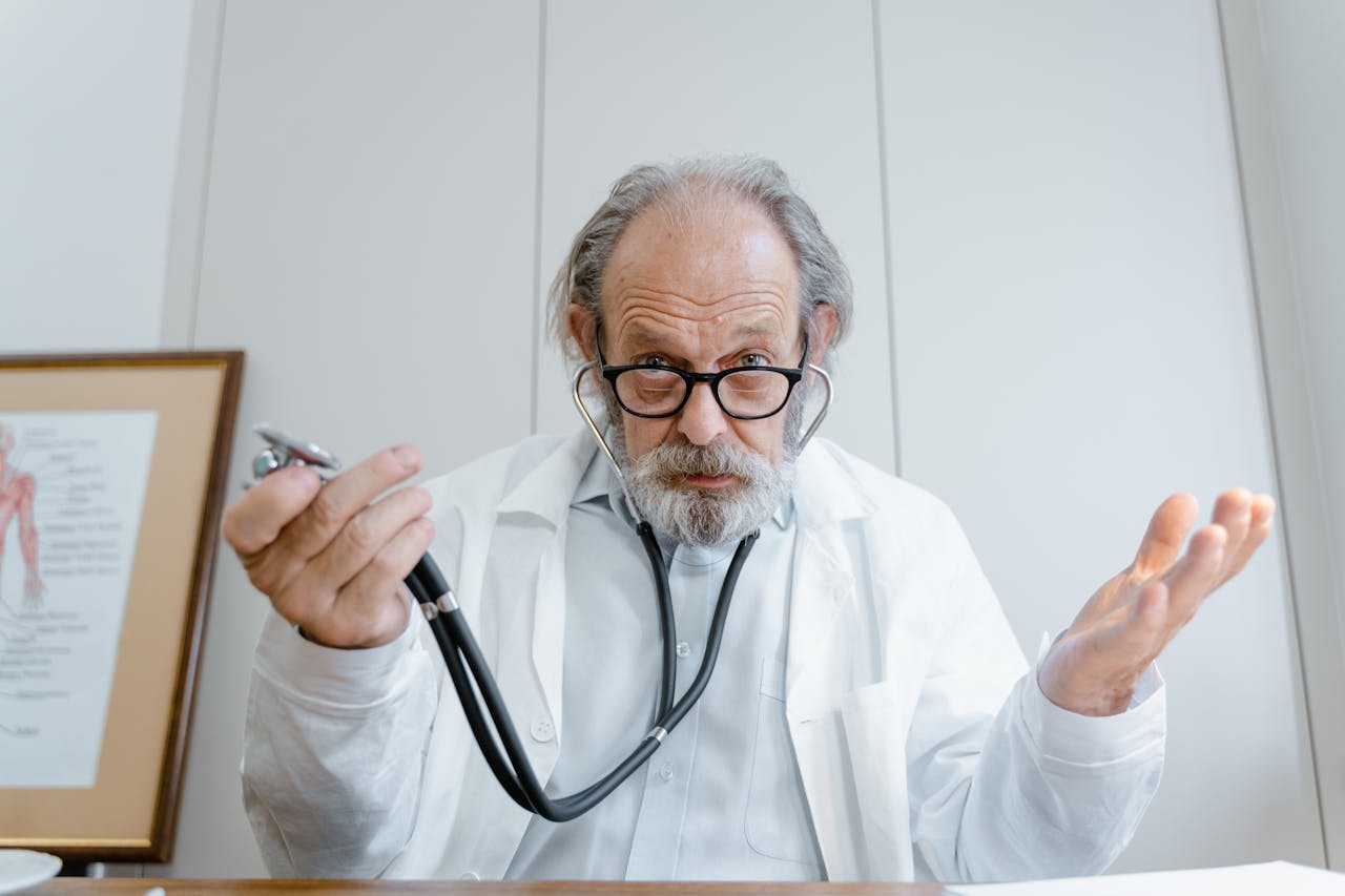 Senior doctor gesturing with stethoscope in a clinical setting, emphasizing telemedicine.